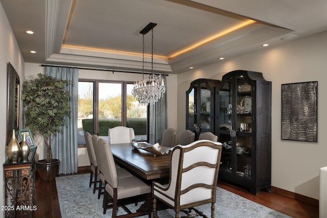 dining space with baseboards, a tray ceiling, recessed lighting, wood finished floors, and a notable chandelier