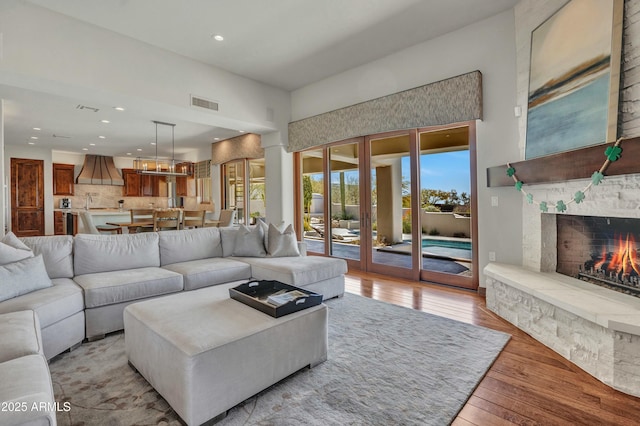 living area featuring visible vents, recessed lighting, light wood-style flooring, a fireplace, and a towering ceiling