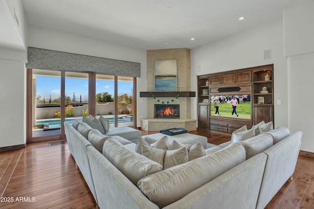 living room with a large fireplace, baseboards, recessed lighting, a towering ceiling, and wood-type flooring