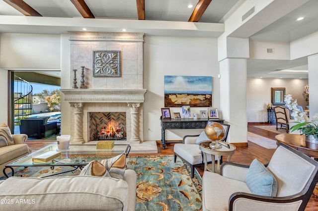 living area featuring visible vents, beamed ceiling, wood finished floors, a premium fireplace, and baseboards