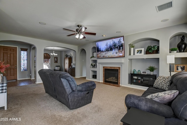 1527 Bainbridge Ln, Chino Valley, AZ 86323 - carpeted living room with arched walkways, built in shelves, a ceiling fan, a fireplace with flush hearth, and a chandelier