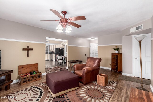 living area featuring ceiling fan with notable chandelier, wood finished floors, visible vents, and baseboards