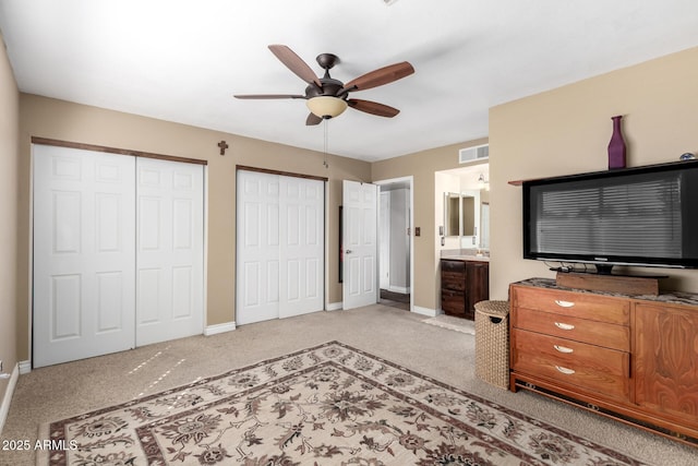 carpeted bedroom featuring two closets, visible vents, a ceiling fan, ensuite bath, and baseboards