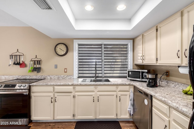 kitchen featuring appliances with stainless steel finishes, a tray ceiling, light countertops, and a sink