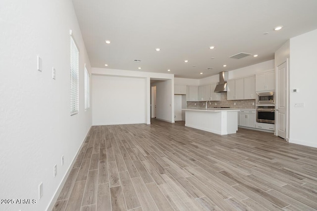 352 E Las Perlas Ln, San Tan Valley, AZ 85140 - kitchen with appliances with stainless steel finishes, wall chimney exhaust hood, light wood-type flooring, light countertops, and tasteful backsplash