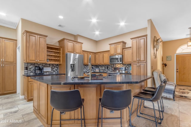 kitchen with appliances with stainless steel finishes, a center island with sink, decorative backsplash, and a kitchen breakfast bar