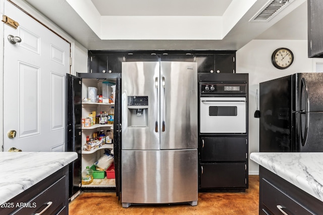 kitchen featuring visible vents, light stone counters, dark cabinets, freestanding refrigerator, and stainless steel refrigerator with ice dispenser