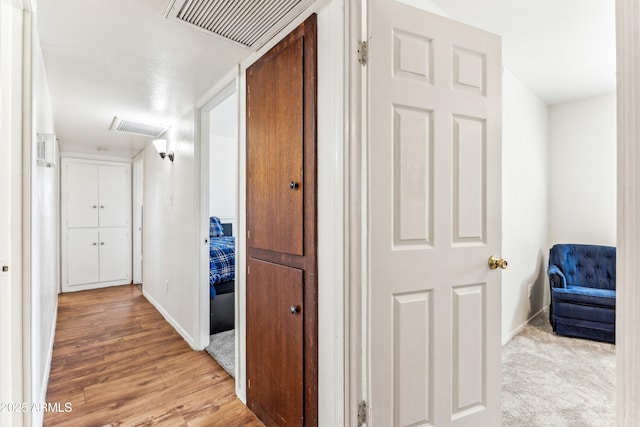 hallway featuring baseboards, light wood finished floors, visible vents, and attic access