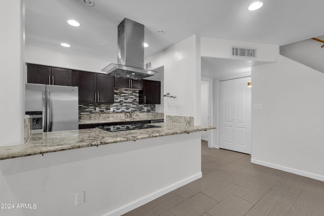 kitchen featuring light stone counters, stainless steel refrigerator with ice dispenser, kitchen peninsula, island exhaust hood, and decorative backsplash