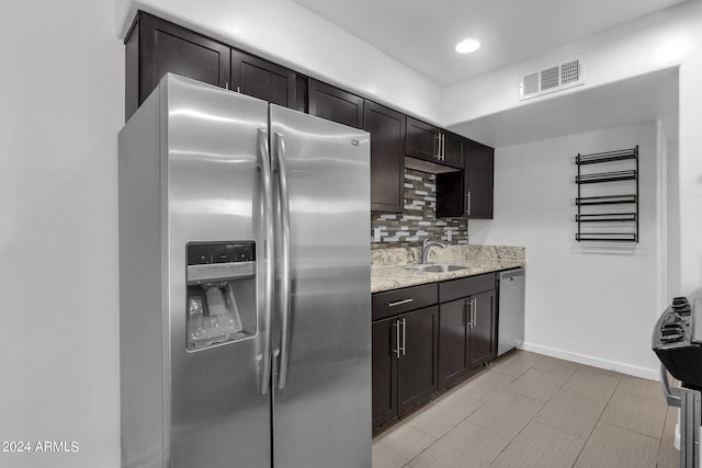 kitchen featuring light stone counters, sink, dark brown cabinets, backsplash, and stainless steel appliances