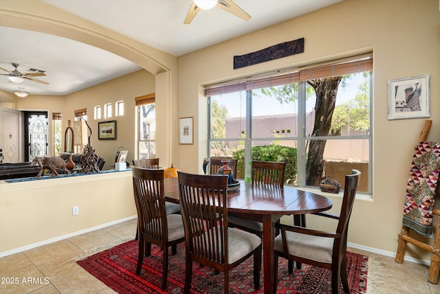 dining room with light tile patterned flooring, a ceiling fan, baseboards, and arched walkways