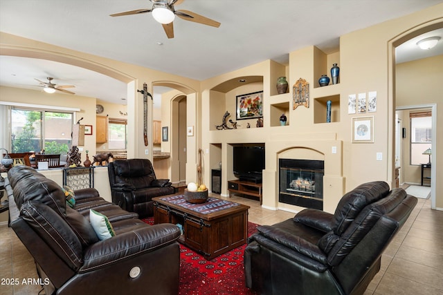 living area featuring tile patterned flooring, built in shelves, arched walkways, and ceiling fan