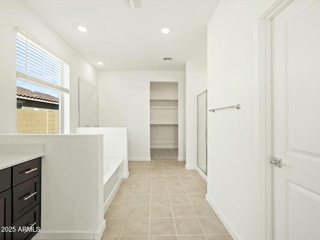 bathroom featuring tile patterned flooring, recessed lighting, a spacious closet, and a garden tub