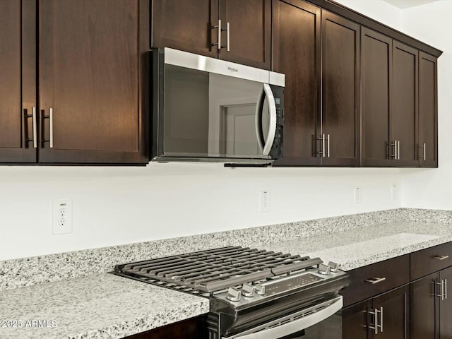 kitchen featuring dark brown cabinetry, stainless steel microwave, gas stove, and light stone counters