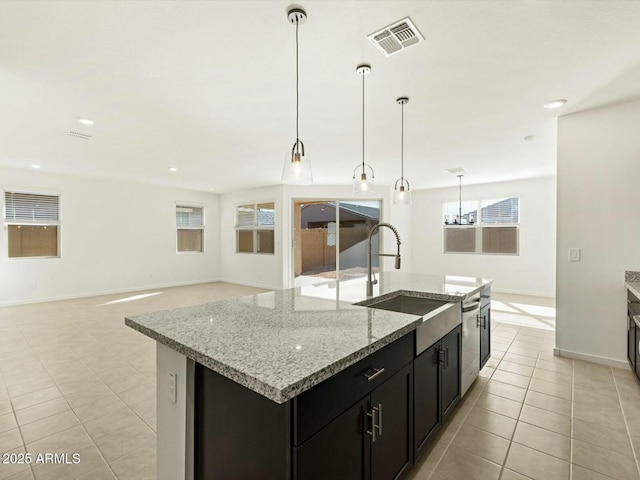 kitchen with visible vents, an island with sink, dark cabinetry, light tile patterned flooring, and a sink