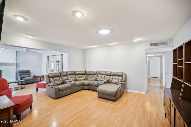 living room featuring a brick fireplace, light wood-type flooring, and ceiling fan