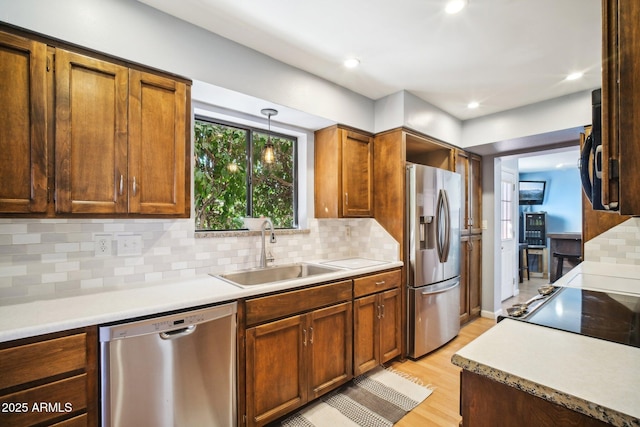 kitchen featuring stainless steel appliances, light wood-type flooring, sink, decorative light fixtures, and backsplash