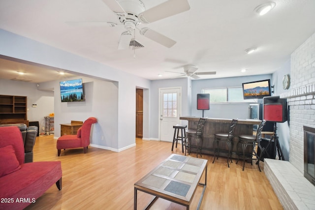 living room with ceiling fan, indoor bar, light hardwood / wood-style flooring, and a brick fireplace