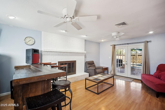 living room with french doors, a brick fireplace, ceiling fan, and light hardwood / wood-style floors