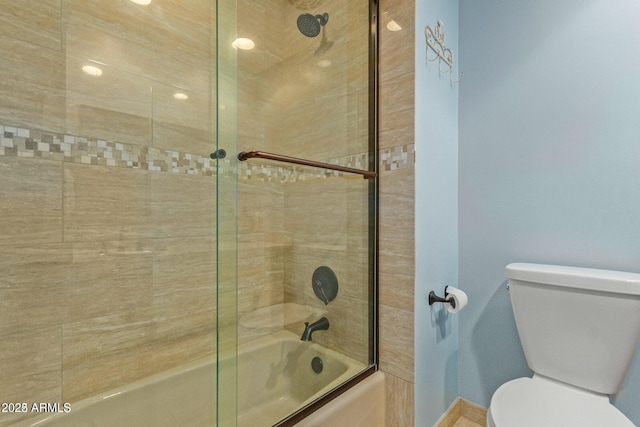 bathroom featuring toilet and bath / shower combo with glass door