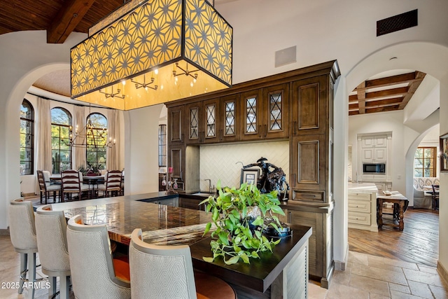 27256 N 97th Pl, Scottsdale, AZ 85262 - bar featuring dark brown cabinetry, a chandelier, black microwave, beamed ceiling, and decorative backsplash