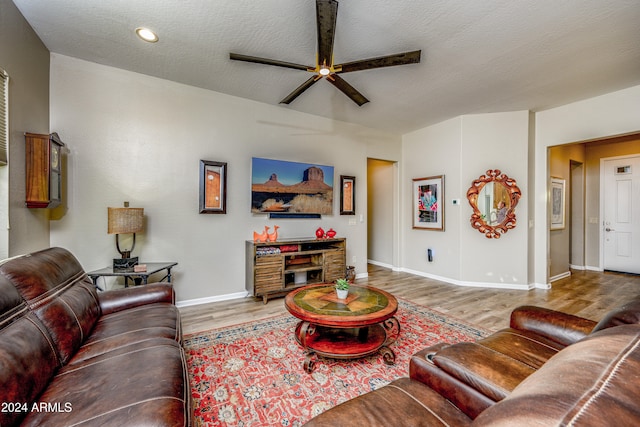 living room with ceiling fan, a stone fireplace, hardwood / wood-style floors, and a textured ceiling