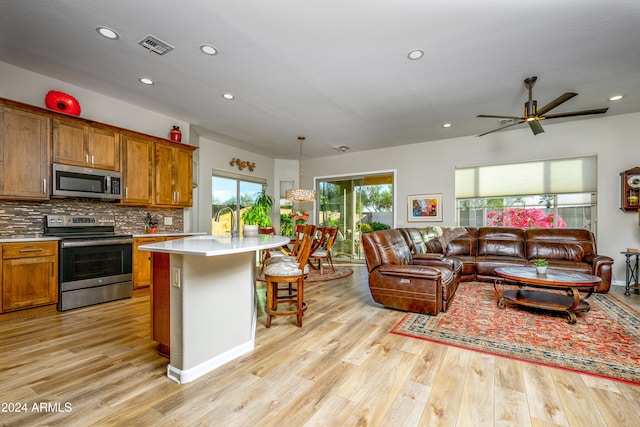 kitchen featuring hanging light fixtures, stainless steel appliances, light wood-type flooring, a kitchen island with sink, and a kitchen breakfast bar