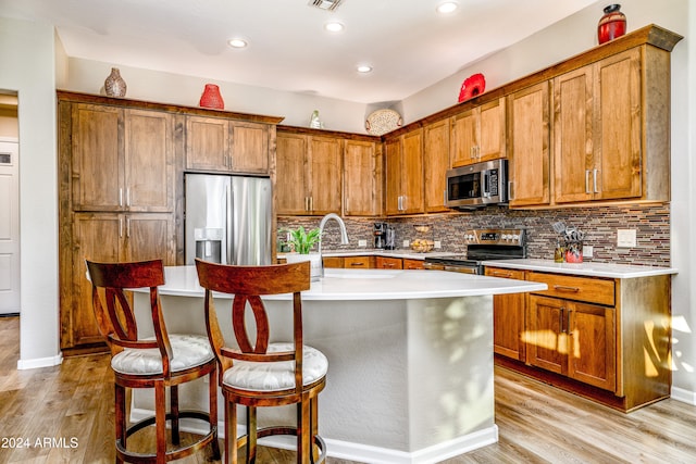 kitchen featuring appliances with stainless steel finishes, light hardwood / wood-style flooring, an island with sink, and a breakfast bar area