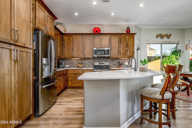 kitchen with stainless steel appliances, sink, a kitchen island with sink, and light wood-type flooring