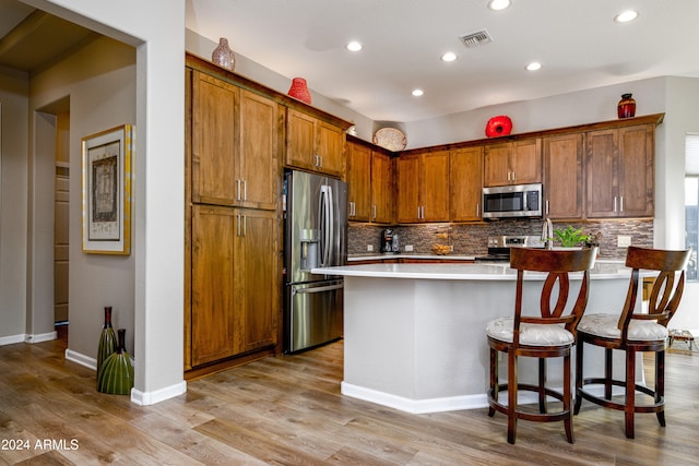 kitchen featuring light wood-type flooring, appliances with stainless steel finishes, decorative backsplash, and a kitchen bar