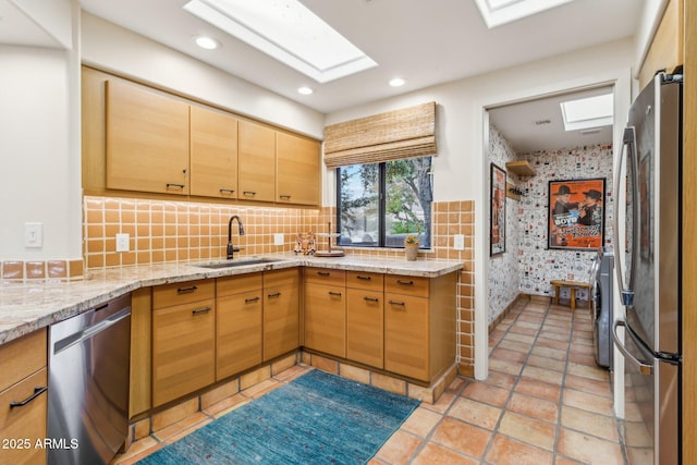 kitchen featuring sink, a skylight, light stone countertops, tasteful backsplash, and stainless steel appliances