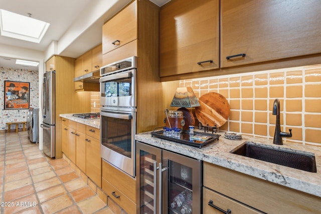 kitchen with light stone countertops, appliances with stainless steel finishes, wine cooler, and sink