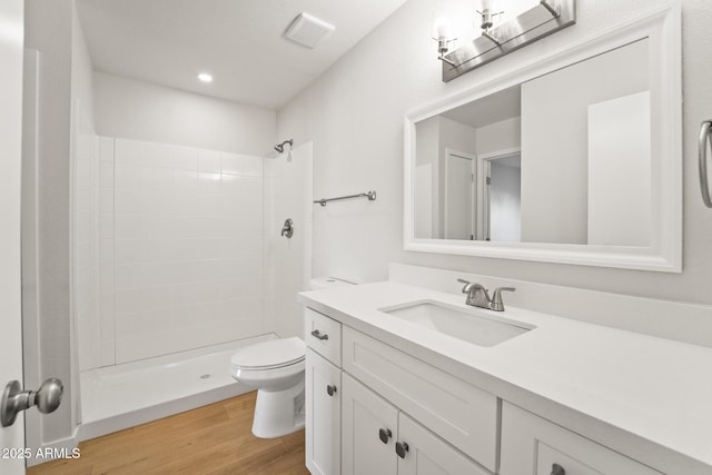 bathroom featuring toilet, tiled shower, wood finished floors, and visible vents