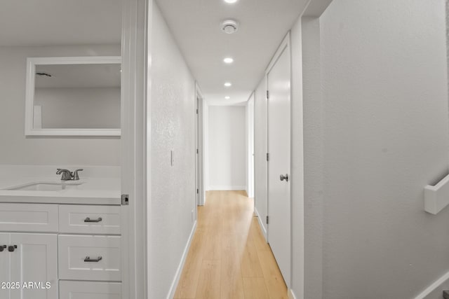 hall featuring visible vents, baseboards, recessed lighting, a sink, and light wood finished floors