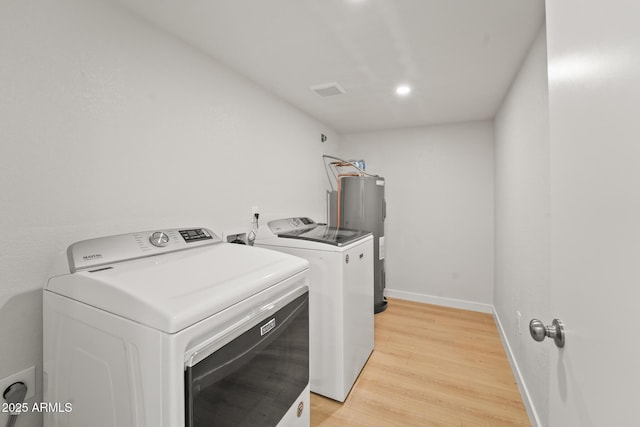 laundry room with laundry area, washer and dryer, baseboards, electric water heater, and light wood-style flooring