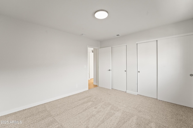 unfurnished bedroom featuring multiple closets, baseboards, carpet, and visible vents