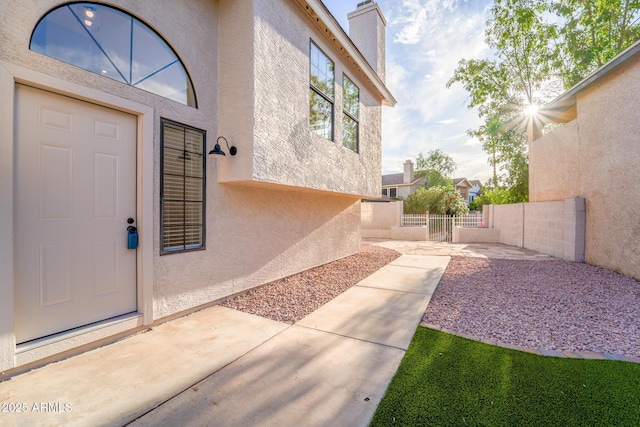 entrance to property featuring a patio area, stucco siding, a chimney, and fence