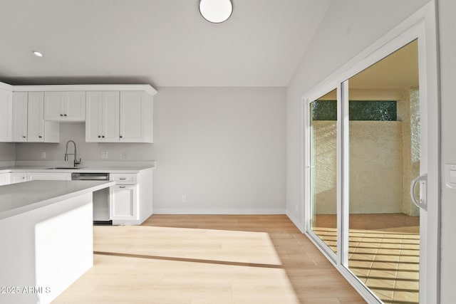 kitchen featuring stainless steel dishwasher, light wood-style floors, light countertops, white cabinets, and a sink