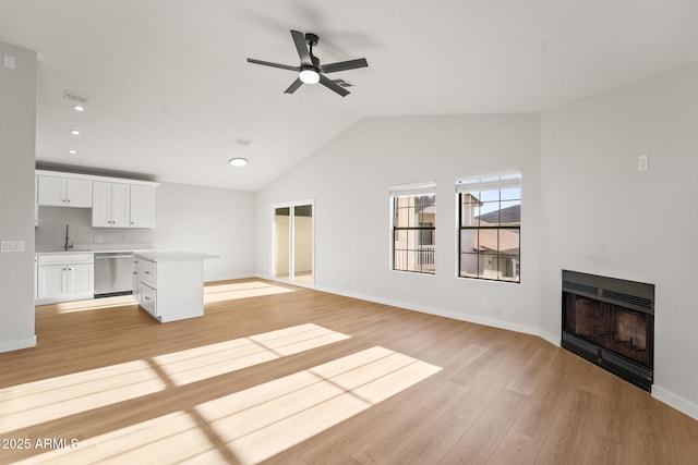 unfurnished living room with a sink, a fireplace, a ceiling fan, light wood-type flooring, and vaulted ceiling