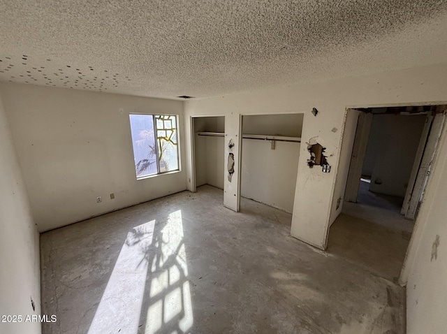 unfurnished bedroom with two closets and a textured ceiling