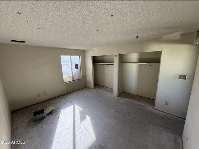 unfurnished bedroom with a textured ceiling and multiple closets