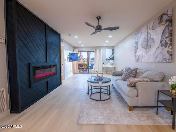 living room featuring a large fireplace, ceiling fan, and light wood-type flooring