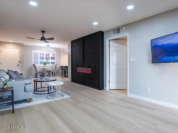 living room featuring light hardwood / wood-style flooring, a large fireplace, and ceiling fan