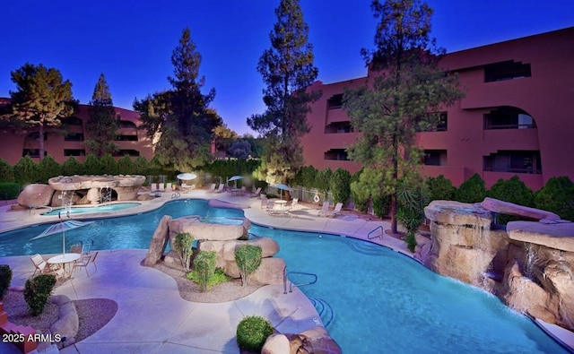 pool at dusk featuring a hot tub, a patio, and pool water feature