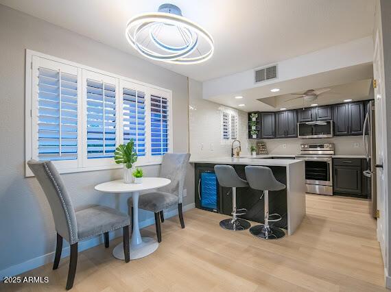 kitchen featuring sink, a breakfast bar area, kitchen peninsula, stainless steel appliances, and light hardwood / wood-style flooring