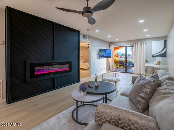 living room with a fireplace, ceiling fan, and light wood-type flooring