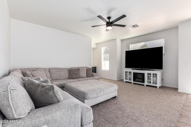 living room with carpet, ceiling fan, visible vents, and baseboards