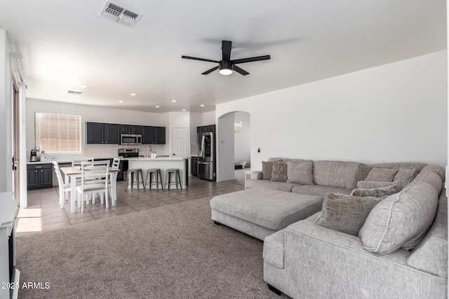 living area with light tile patterned floors, visible vents, arched walkways, light colored carpet, and ceiling fan