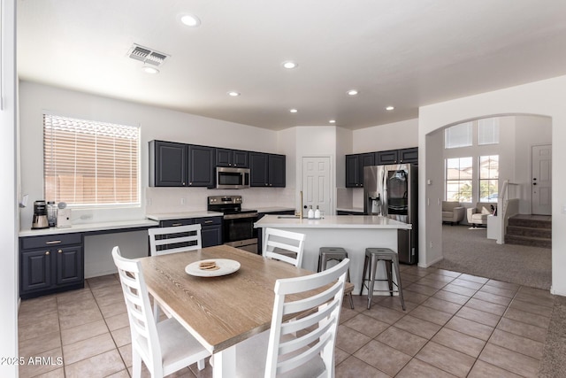 kitchen with arched walkways, stainless steel appliances, light countertops, and a center island