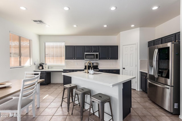 kitchen featuring a breakfast bar, light tile patterned floors, stainless steel appliances, a sink, and an island with sink